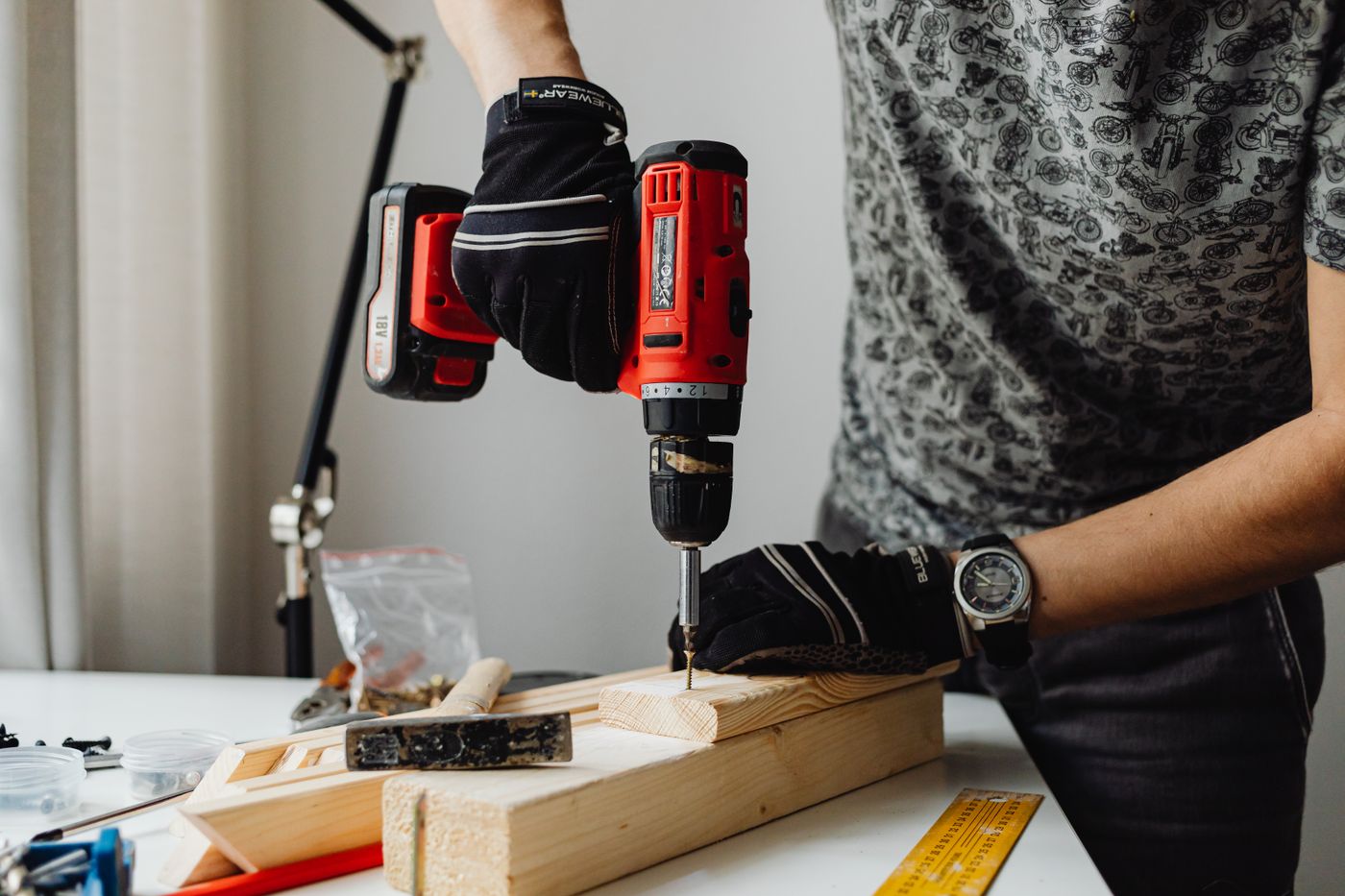 A person in work gloves driving a screw into a pine board with a cordless drill